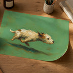 A rectangular green placemat or art print featuring a painted running dog, styled on a wooden desk with a cup of coffee, notebook, pen, and other desk accessories.