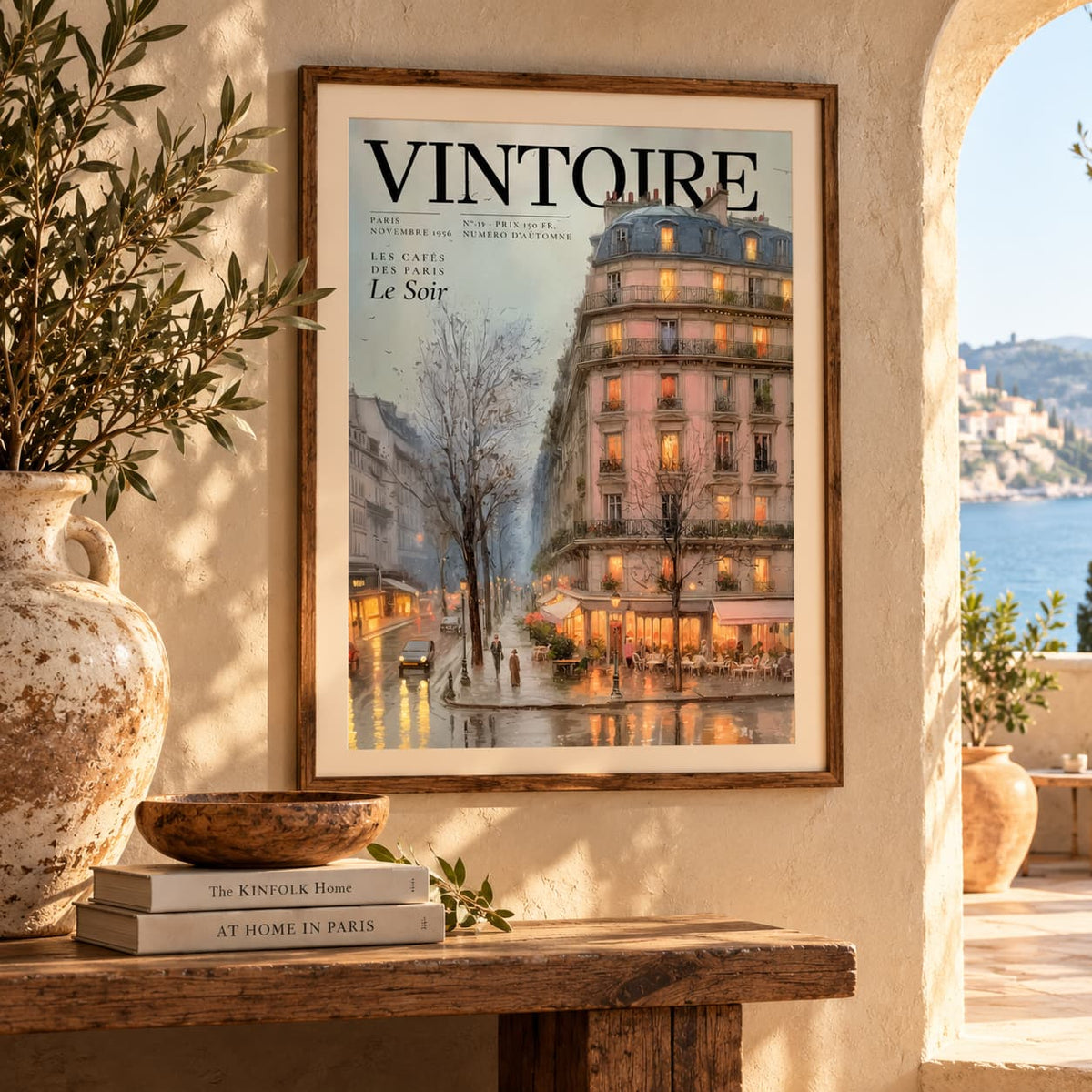 A framed vintage-style poster or magazine cover print hanging on a beige wall in a sunlit interior. The artwork shows a Parisian street scene with a large lit building, trees, and the title 'VINTOIRE' at the top.